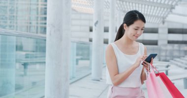 Kadın cep telefonu ve alışveriş çantası kullanıyor.
