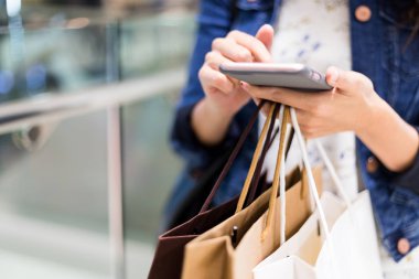 Kadın elinde cep telefonu ve kağıt çanta alışveriş merkezinde alışveriş 