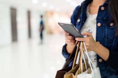 Asya alışveriş torbaları tutarak ve smartphone kullanarak kadın 