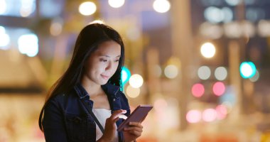 Genç kadın cep telefonuyla şehirde geceleri