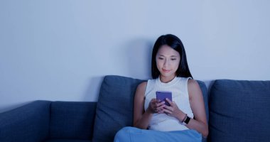 Kadın akıllı telefondan arıyor ve evdeki kanepede oturuyor. 