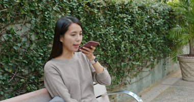 Cep telefonu kullanıp parkta oturan bir kadın.