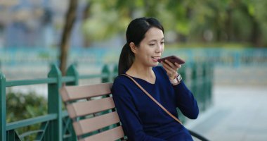 Genç kadın cep telefonunuzun söz ve parkta oturmak