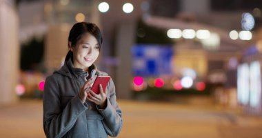 Geceleri sokakta yer aramak için cep telefonu kullanan kadın