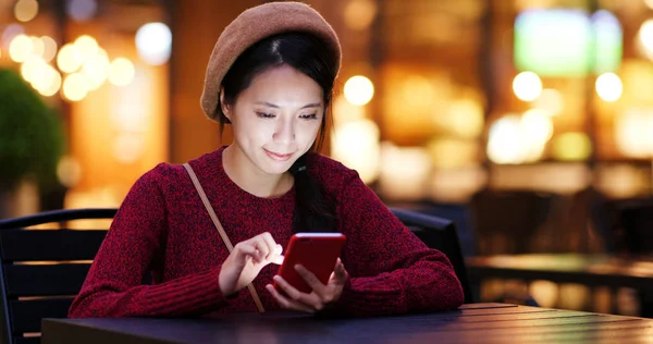 Woman using smartphone at outdoor coffee shop at night