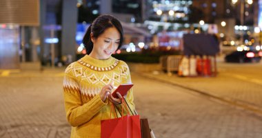 Cep telefonu kullaranarak ve alışveriş torbaları geceleri tutan kadın