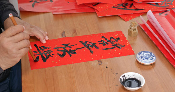 Old man pratice on writing Chinese calligraphy for lunar new year words means happy new year