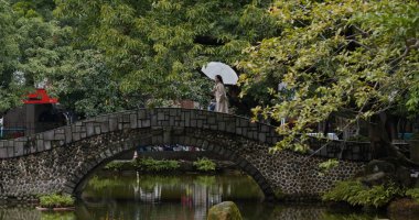 Kadın parktaki taş köprüde yürüyor.