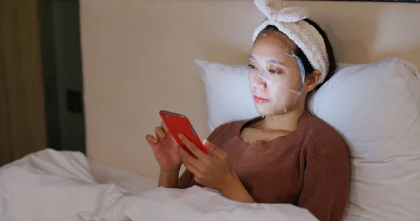 Wanita Menggunakan Ponsel Dan Mengenakan Masker Wajah Tempat Tidur Malam — Stok Foto