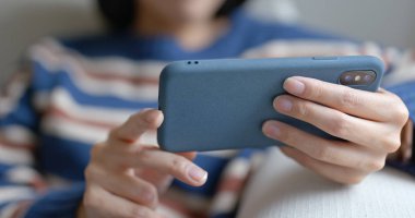 Kadın cep telefonuyla izleyip evdeki kanepeye oturuyor.