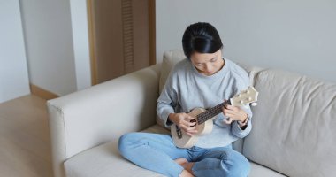 Kadın evde ukulele ile oynuyor.