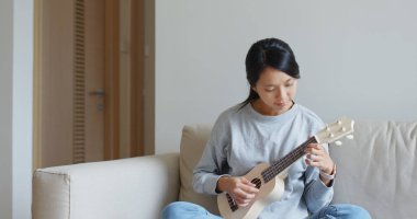 Kadın evde ukulele ile oynuyor.