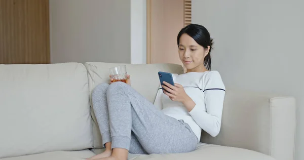 Woman enjoy use of mobile phone and sit on sofa with holding a cup of tea