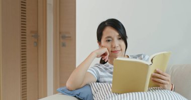 Kadın kitap okuyor ve evdeki kanepeye oturuyor.