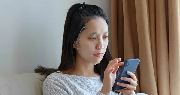 Frau Trägt Gesichtsmaske Auf Und Benutzt Handy Hause — Stockfoto