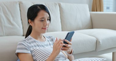 Kadın cep telefonu kullanıyor ve evdeki kanepeye oturuyor.