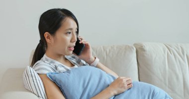 Cep telefonuyla konuşan ve evdeki koltukta oturan bir kadın.