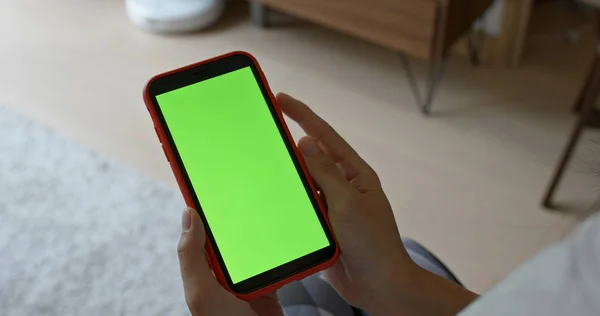 Woman holding cellphone with green screen at home