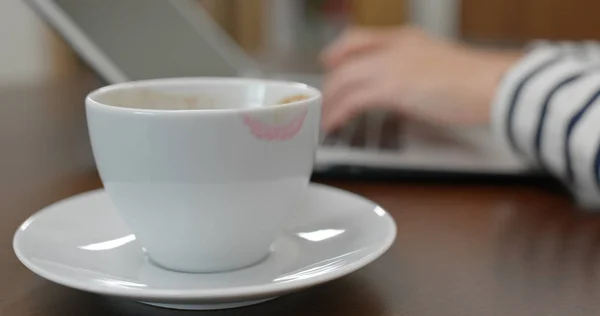 Woman typing of laptop computer, with red lip mark on a coffee cup