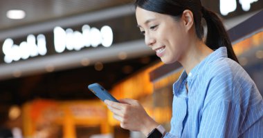 Kadın alışveriş merkezinde cep telefonuyla çalışıyor.