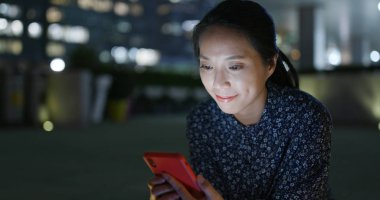 Genç kadın gece şehirde cep telefonu kullanıyor.