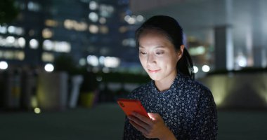 Genç kadın gece şehirde cep telefonu kullanıyor.