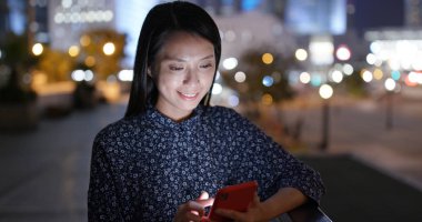 Genç kadın gece şehirde cep telefonu kullanıyor.