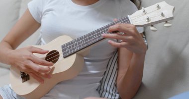 Kadın evde ukulele çalışıyor.