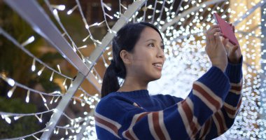 Kadın cep telefonuyla gece dekorasyonunun arka planında fotoğraf çekiyor.