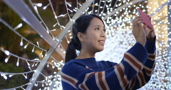 Kadın cep telefonuyla gece dekorasyonunun arka planında fotoğraf çekiyor.