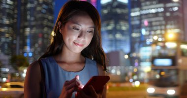 Asyalı kadın geceleri şehir içinde hareket eden telefon bakmak