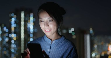 Kadın gece şehirde cep telefonunu kontrol ediyor.