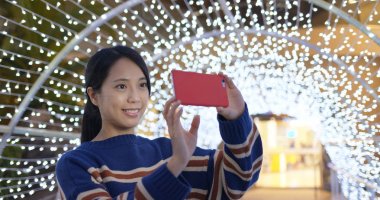 Gece yılbaşı dekorasyonuyla fotoğraf çektirmek için kadın telefonu kullanıyor.