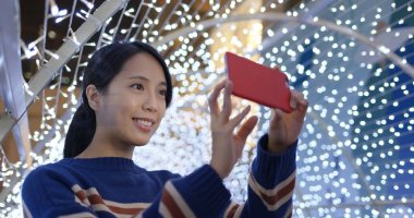 Kadın cep telefonuyla güzel bir noel süslemesiyle gece fotoğraf çekiyor.