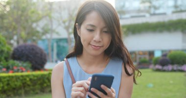 Kadın akıllı telefon kullanıyor ve parkta oturuyor.