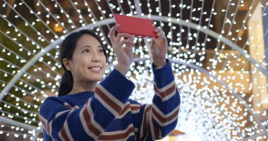 Gece yılbaşı dekorasyonuyla fotoğraf çektirmek için kadın telefonu kullanıyor.