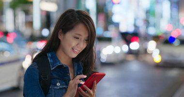 Kadın gece şehirde cep telefonunu kontrol ediyor.