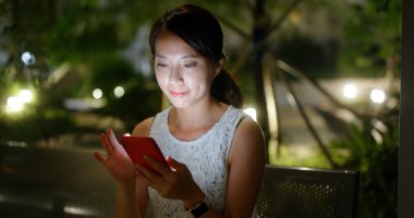 Kadın gece şehirde cep telefonunu kontrol ediyor.