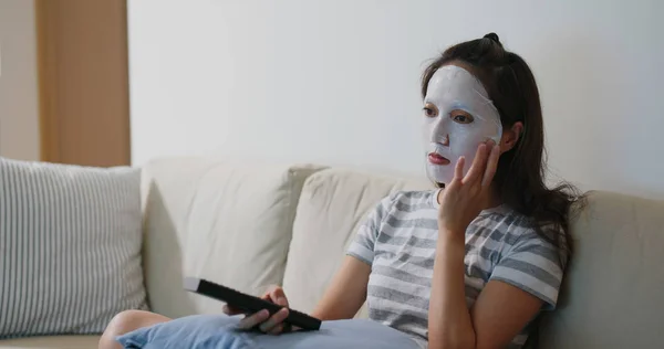 Женщина наносит маску и смотрит телевизор дома — стоковое фото