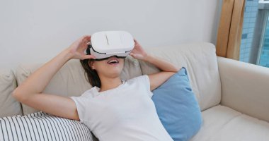 Kadın VR cihazından izliyor ve evdeki kanepede yatıyor.