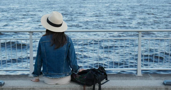 Kobieta siedzi nad morzem i rozgląda się po porcie. — Zdjęcie stockowe