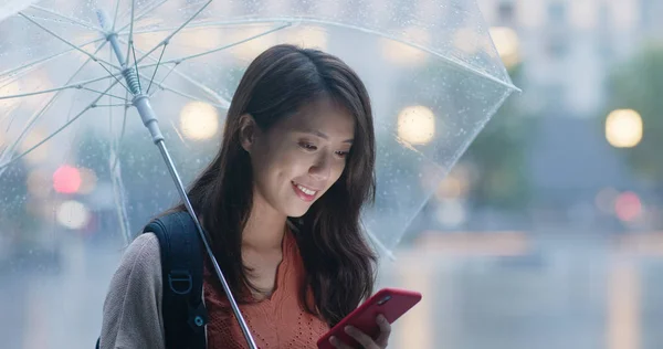 Woman use of mobile phone and hold with umbrella in the evening
