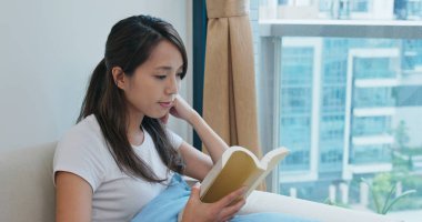 Kadın evde kitap okuyor.