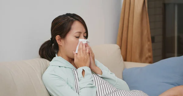 Chora kobieta kicha i siedzi na kanapie w domu — Zdjęcie stockowe