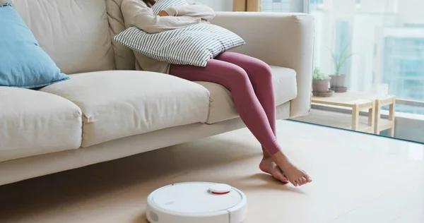女性は家の床にロボット掃除機で足を持ち上げる — ストック写真