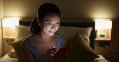 Gece yatakta cep telefonu kullanan bir kadın.