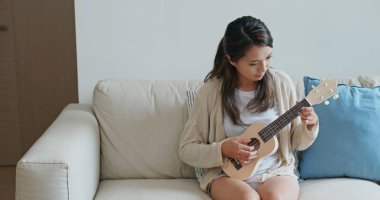 Kadın evde ukulele ile oynuyor.