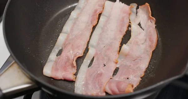 Stekt bacon i kastrull i köket till frukost — Stockfoto