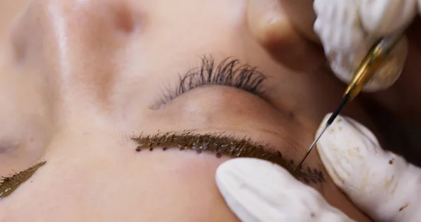 Cosmetologist applying permanent tattooing of eyebrows in beauty