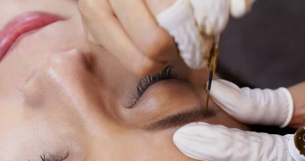 Cosmetologist applying permanent tattooing of eyebrows in beauty